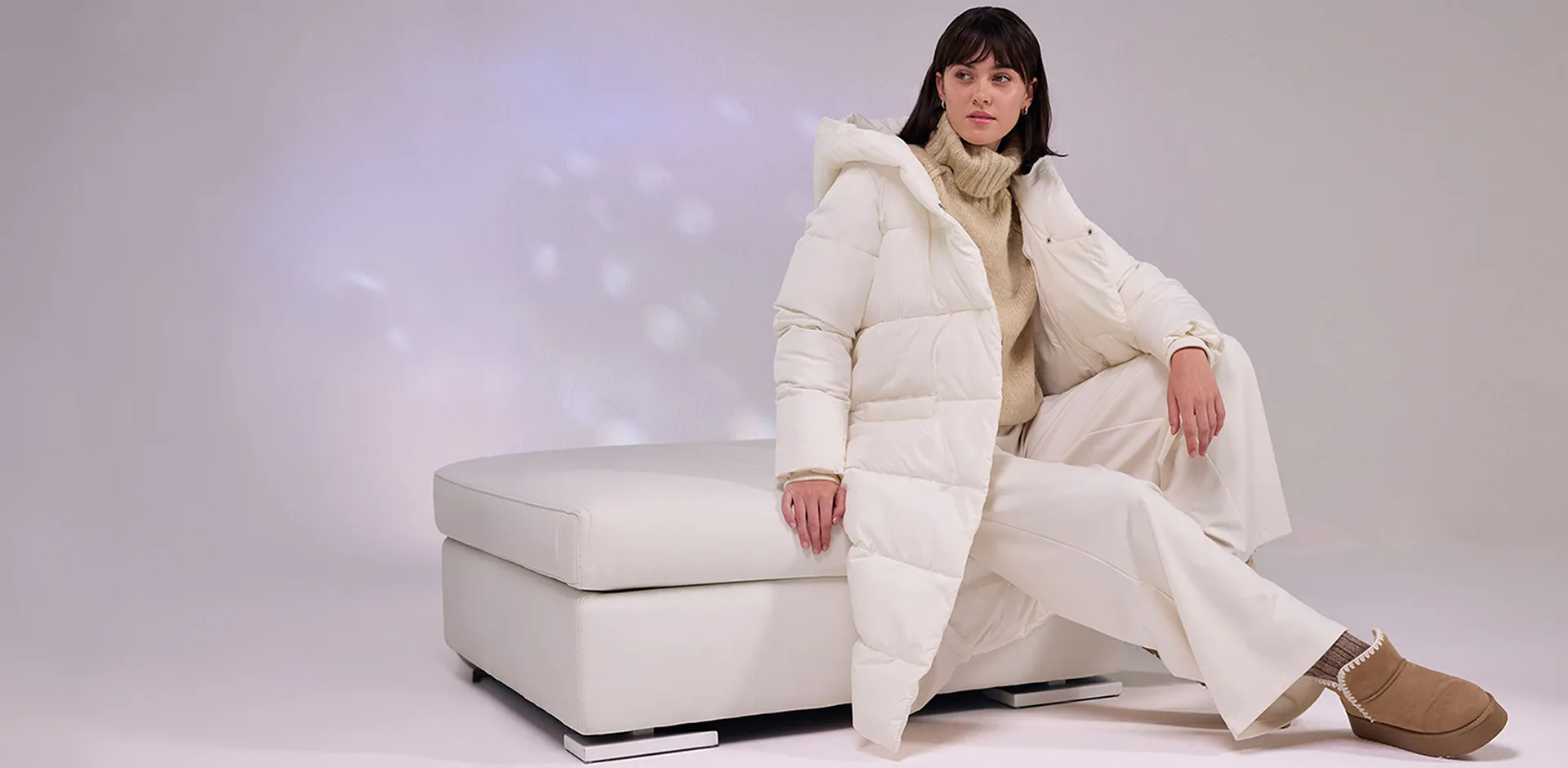 Piumino color crema, pantaloni bianchi e stivali morbidi.