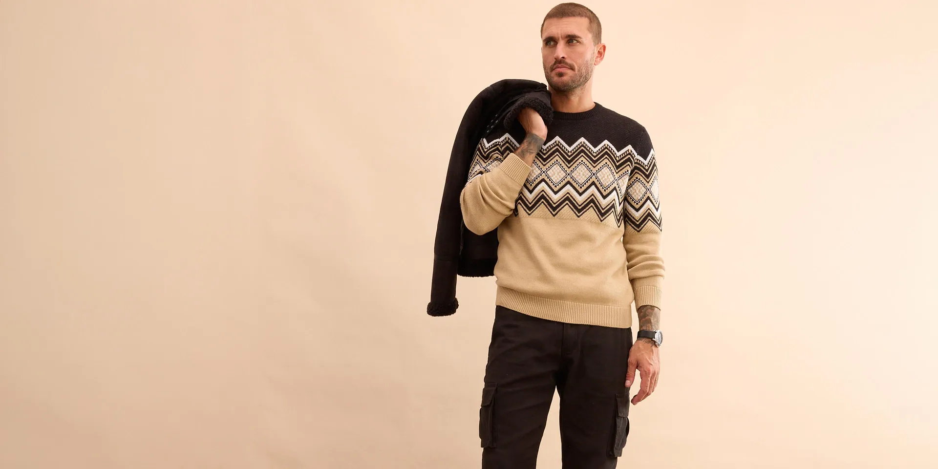 Look elegante con giacca invernale nera, maglione fantasia e jeans per le giornate fredde.