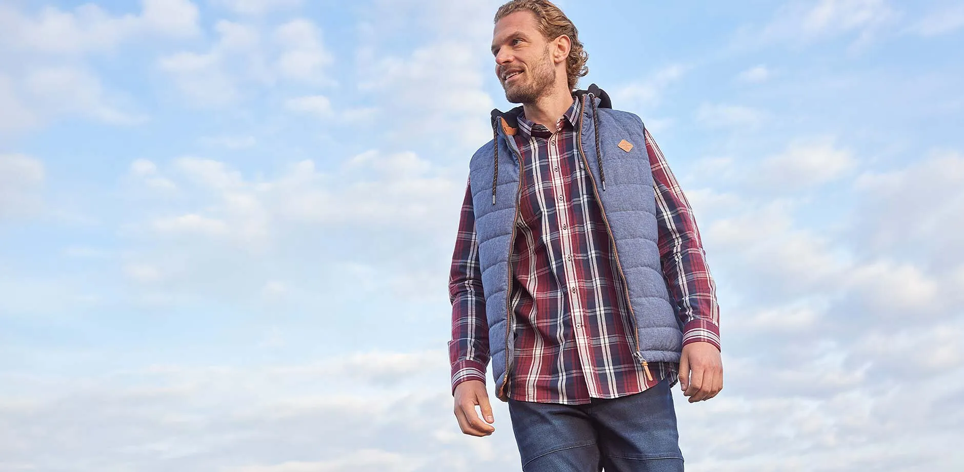 Camicia a quadri, jeans blu e gilet grigio.