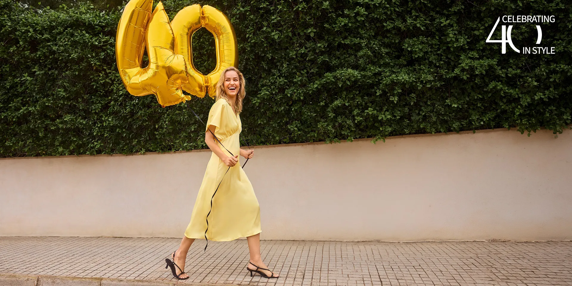 Un abito estivo giallo a maniche corte, completato da eleganti sandali neri.