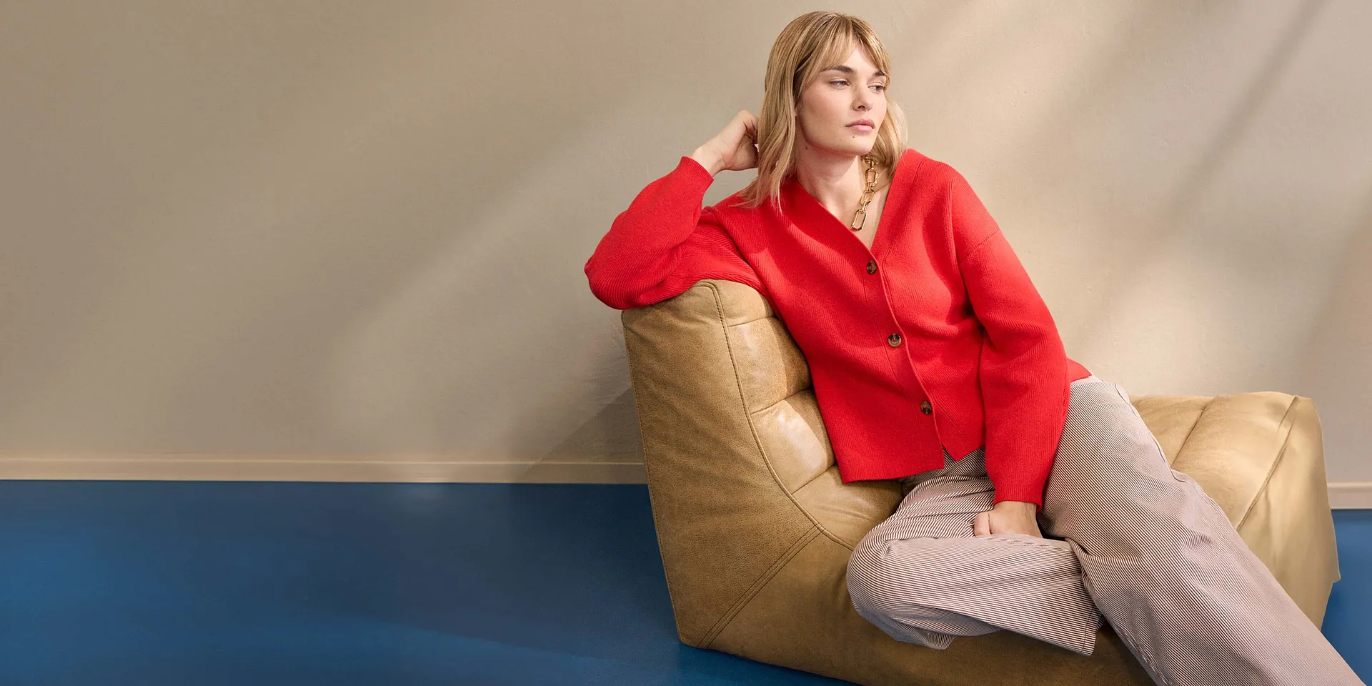 Una donna indossa un cardigan rosso abbinato a pantaloni beige.