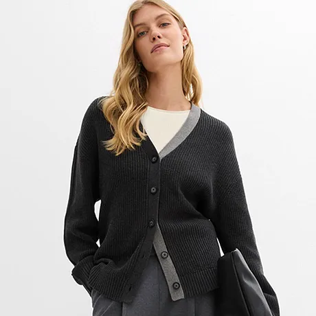 Cardigan scuro lavorato a maglia sopra una camicia bianca, abbinato a una gonna grigia e una borsa nera.