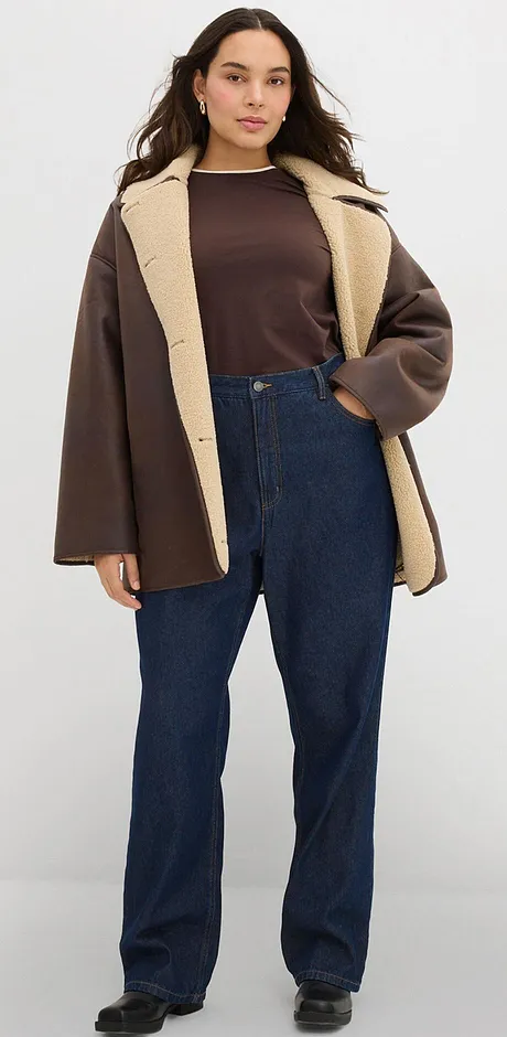 Giacca marrone con colletto chiaro, abbinata a un top scuro e jeans.