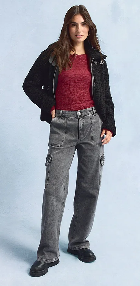 Giacca nera, maglia rossa, jeans larghi grigi e scarpe scure.