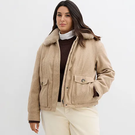 Giacca invernale beige con colletto, sotto un maglione marrone e un dolcevita bianco.