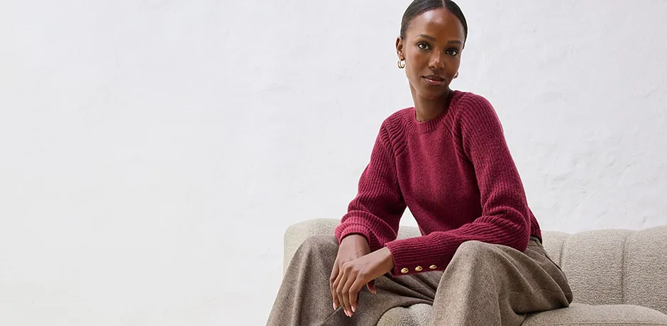 Maglione rosso con pantaloni beige su un divano chiaro.