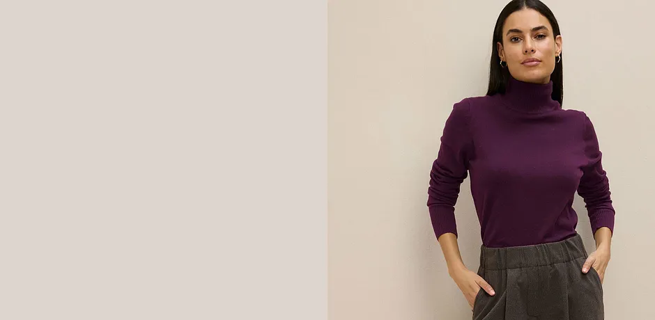 Maglione a collo alto viola abbinato a pantaloni grigi.