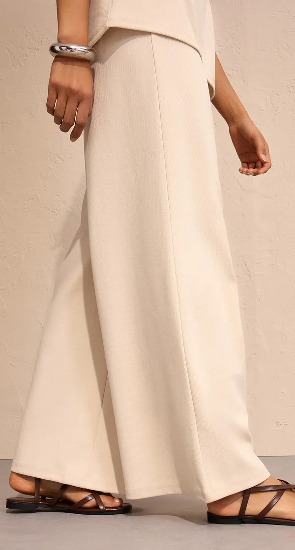 Eleganti pantaloni larghi color bianco crema, abbinati a sandali bassi.