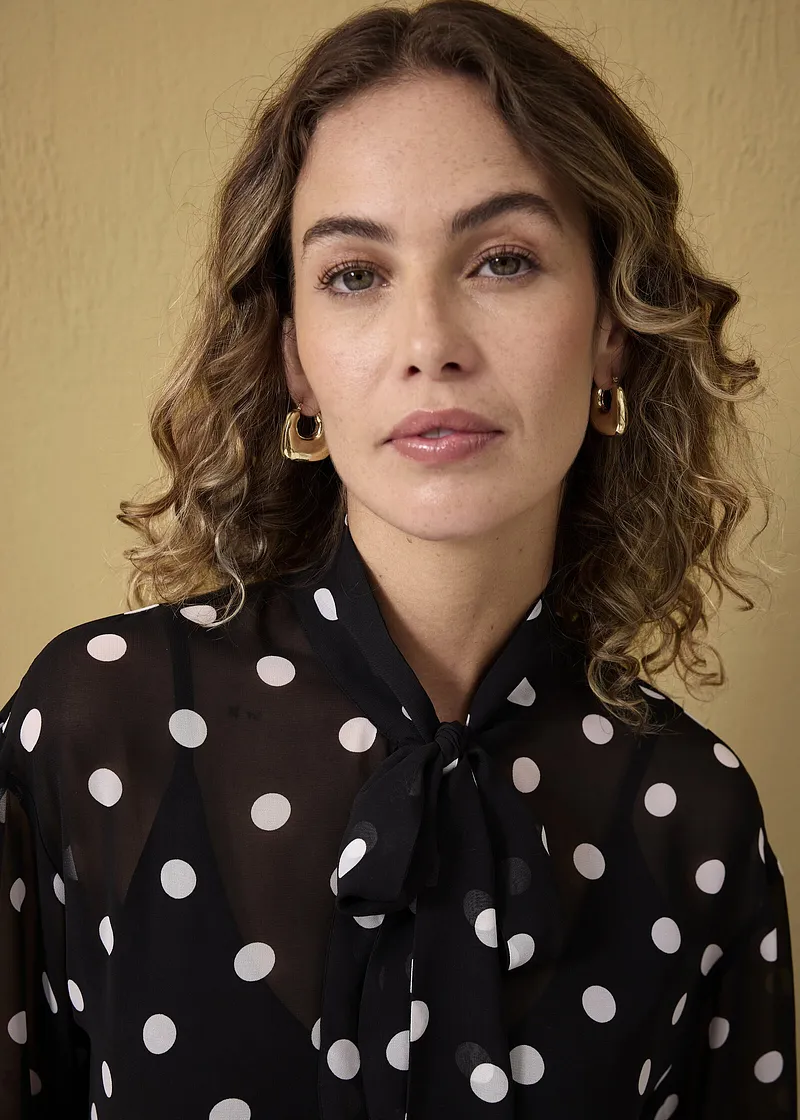 Camicia nera con pois bianchi e colletto con fiocco. Orecchini dorati completano il look.