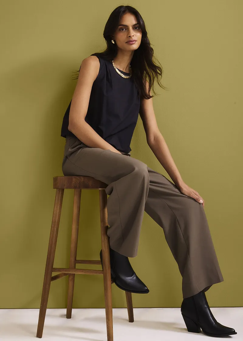 Top senza maniche blu scuro, pantaloni larghi marroni e stivaletti neri. Look elegante e casual.