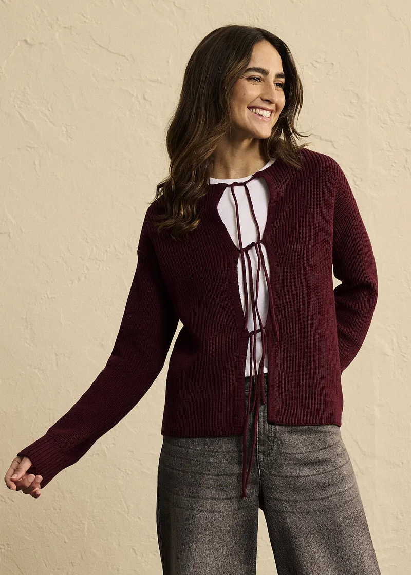 Combinazione di cardigan bordeaux, blusa bianca con laccetti e pantaloni grigi.