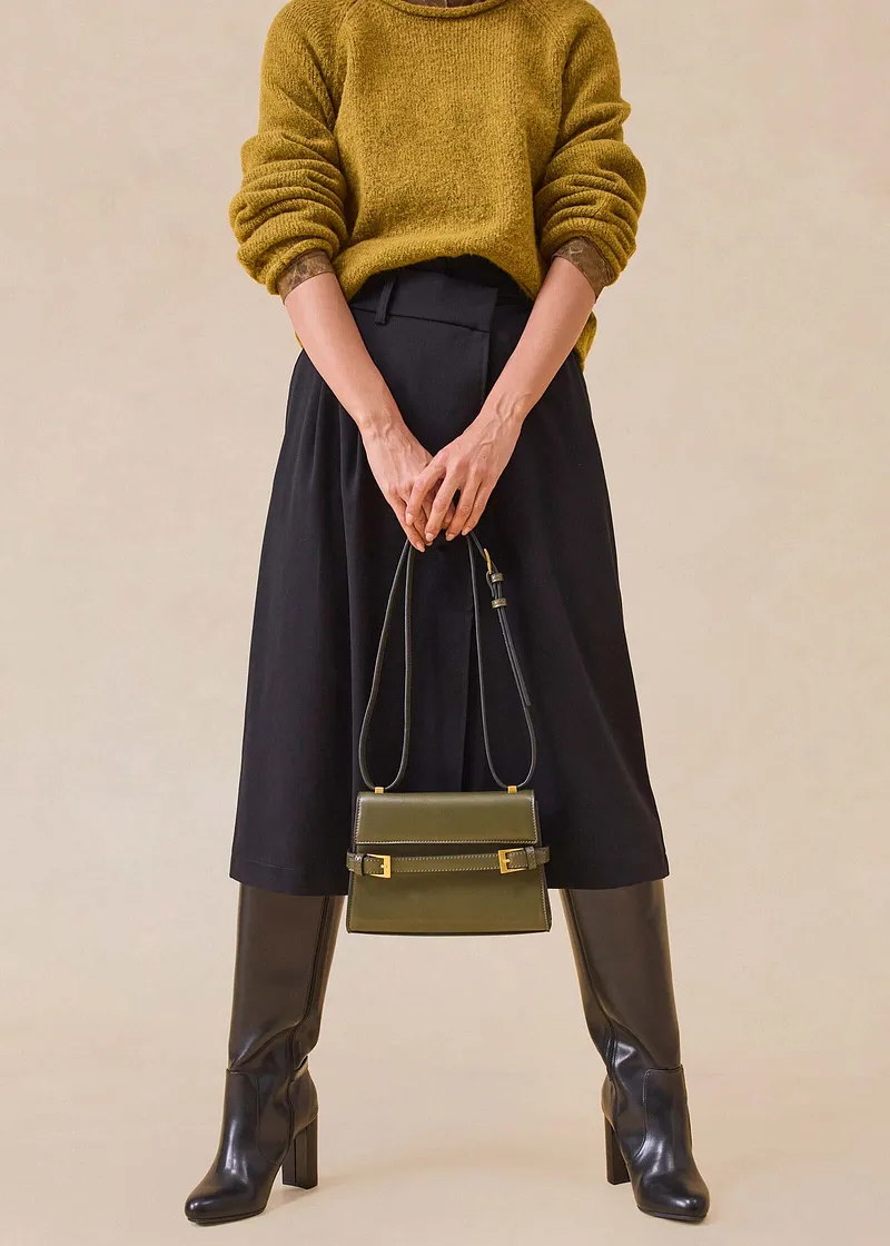 Maglione giallo senape, gonna midi nera, stivali marroni e borsa elegante.