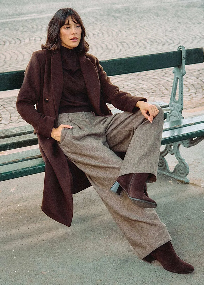 Cappotto lungo marrone, maglione a collo alto e pantaloni larghi in tweed.