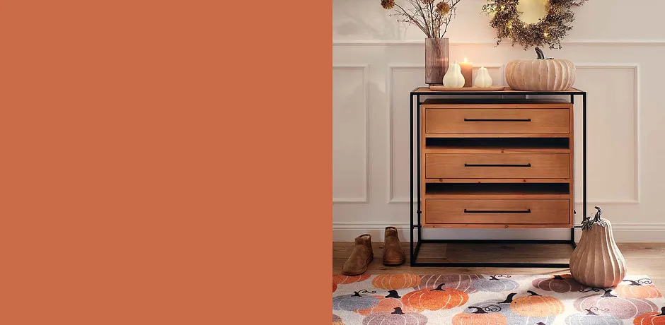 Cassettiera in legno con maniglie nere, circondata da decorazioni autunnali e calde tonalità terrose.