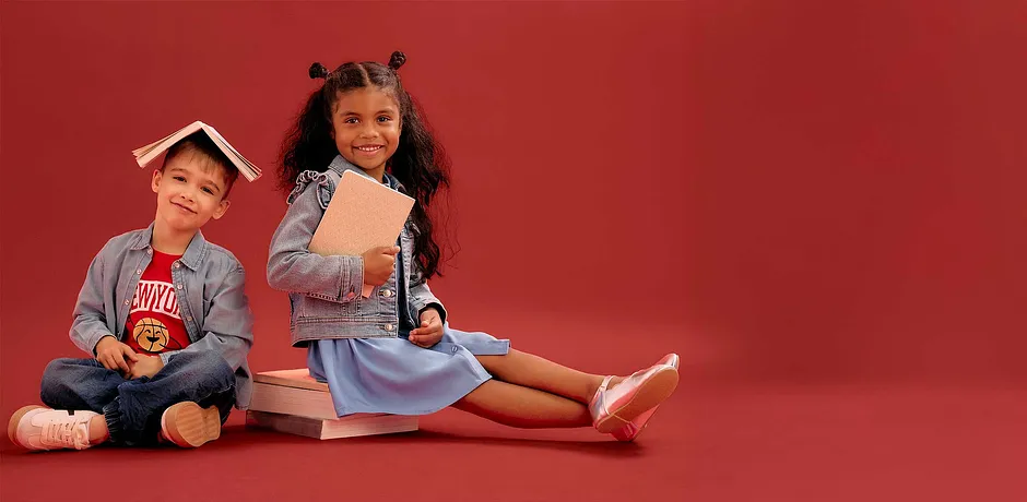 Bambini in abiti casual colorati siedono con libri davanti a uno sfondo rosso. Look casual con magliette e jeans.