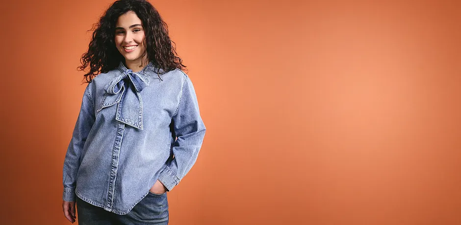 Una camicia di jeans azzurra con fiocco al collo conferisce un fascino casual all'outfit.