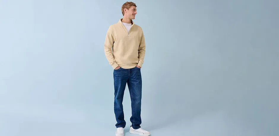 Look casual con maglione color crema, jeans blu e sneakers bianche.