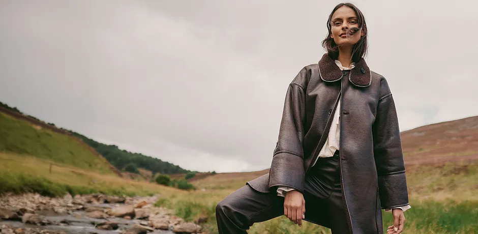 Elegante cappotto in pelle marrone con ampio collo abbinato a un top chiaro e pantaloni scuri.