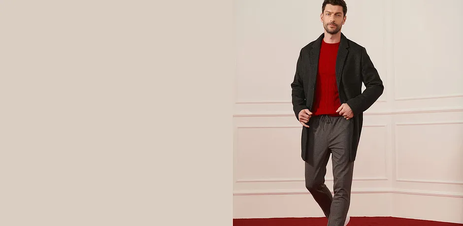 Cappotto di lana scuro, maglione rosso e pantaloni grigi per un look elegante.