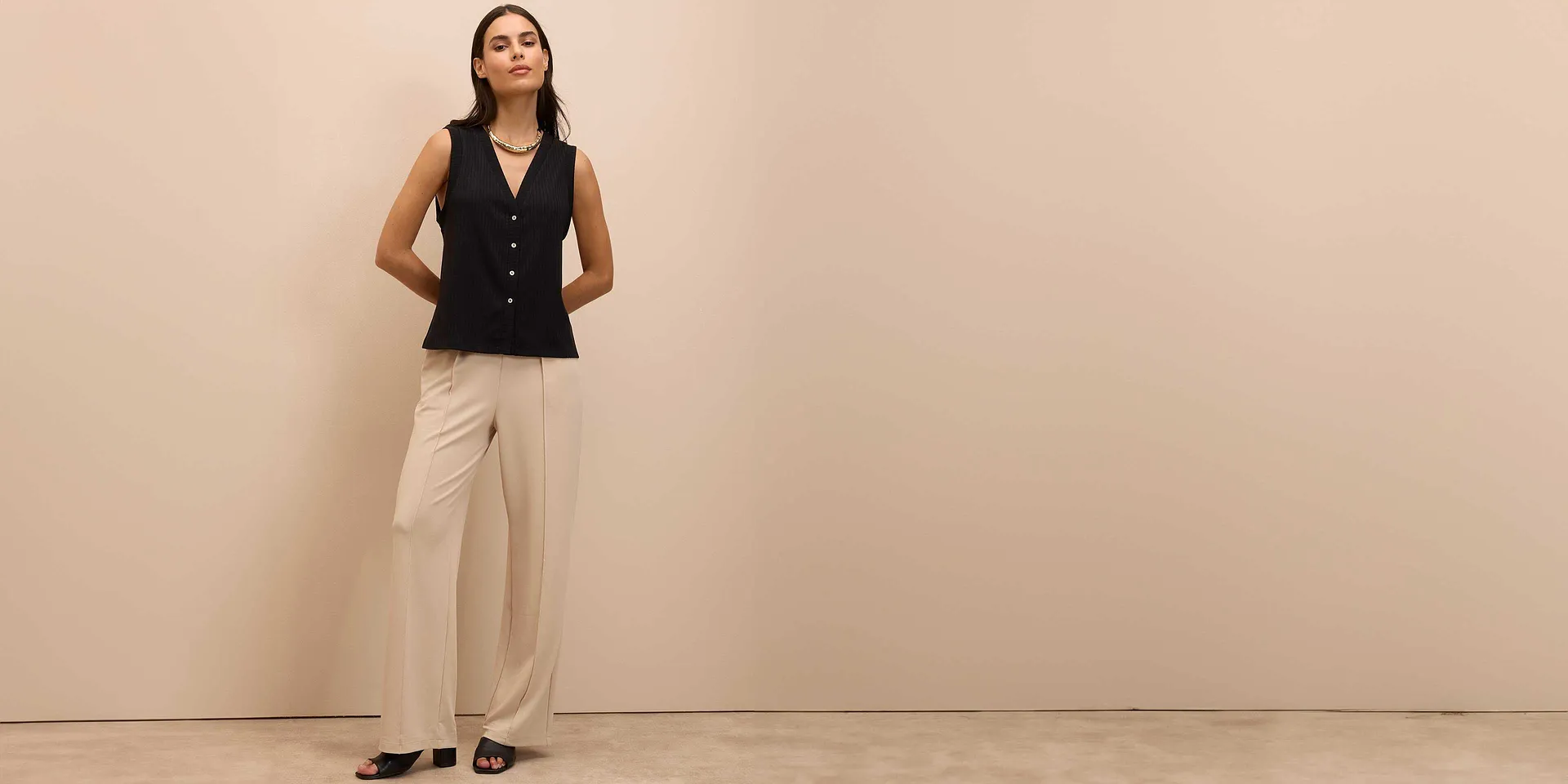 Elegante gilet nero con bottoni, abbinato a ampi pantaloni beige e scarpe nere.