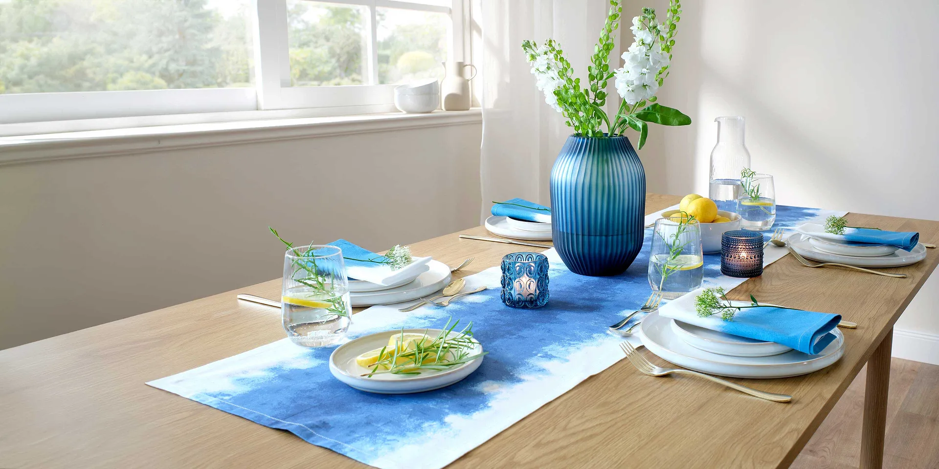 Un runner da tavolo blu decora il tavolo da pranzo, in contrasto con piatti bianchi e accessori colorati.