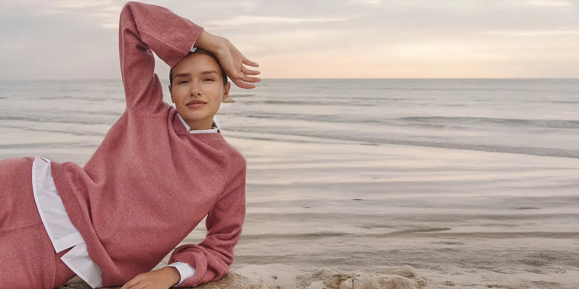 Donna con maglione rosa con cappuccio in riva al mare, look comodo da casa.