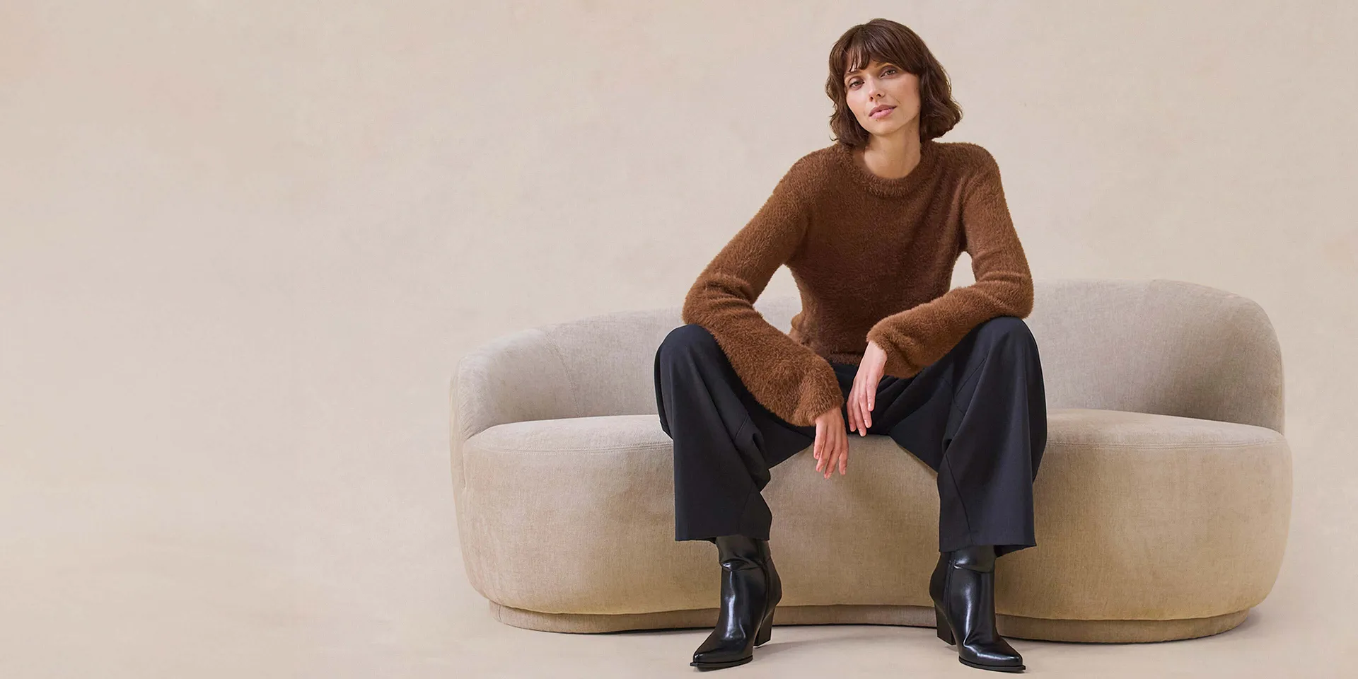 Elegante maglione marrone, pantaloni larghi e stivali neri.