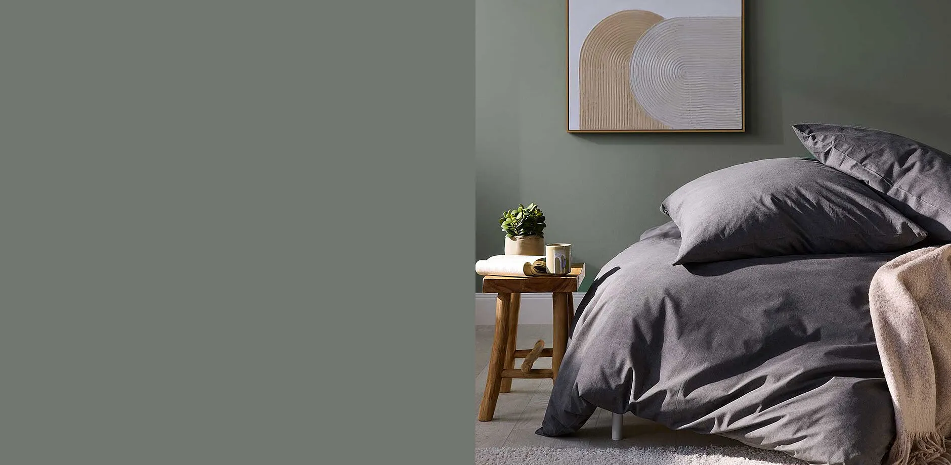 Biancheria da letto grigia elegante che si armonizza bene alla parete verde. Una pianta completa l'ambiente minimalista.