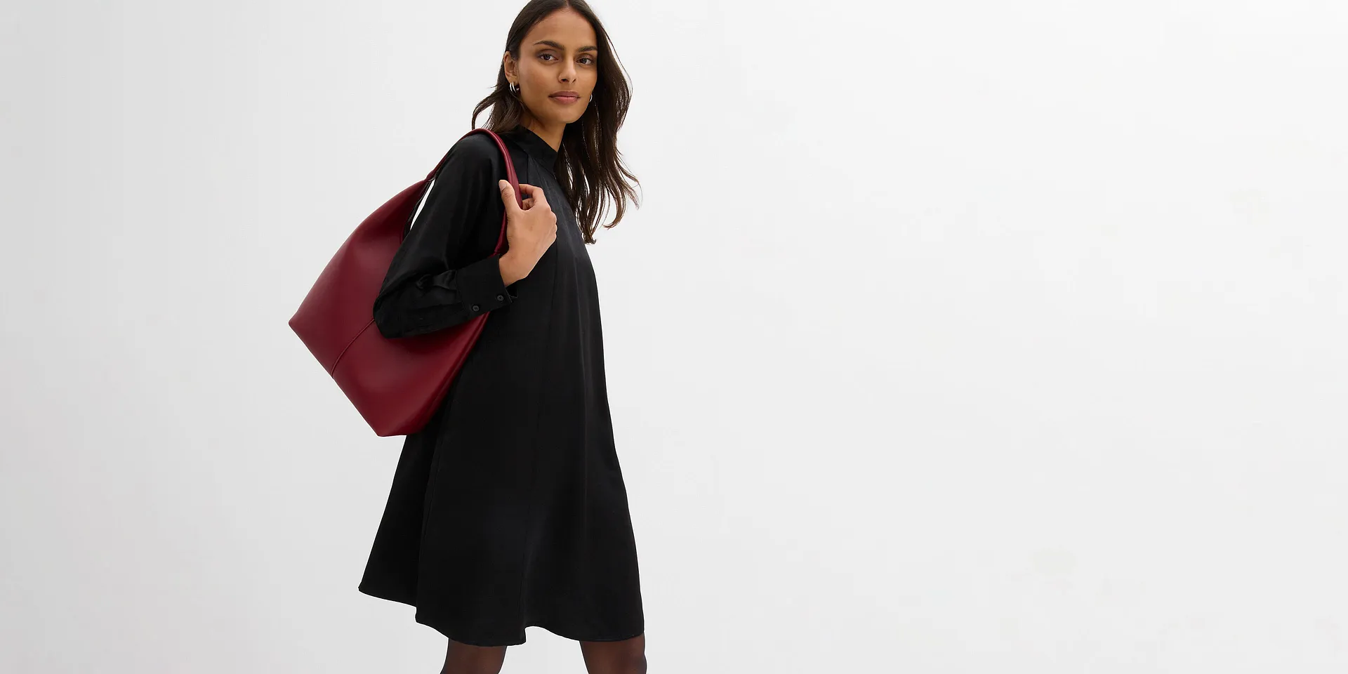 Abito nero corto a maniche lunghe, con collo alto e decorazione bianca sul colletto.