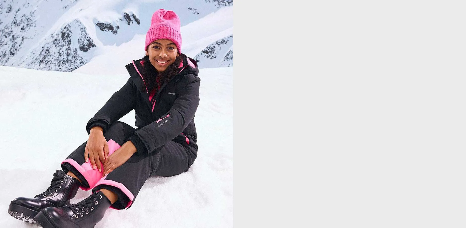 Giacca e pantaloni invernali neri, berretto rosa.