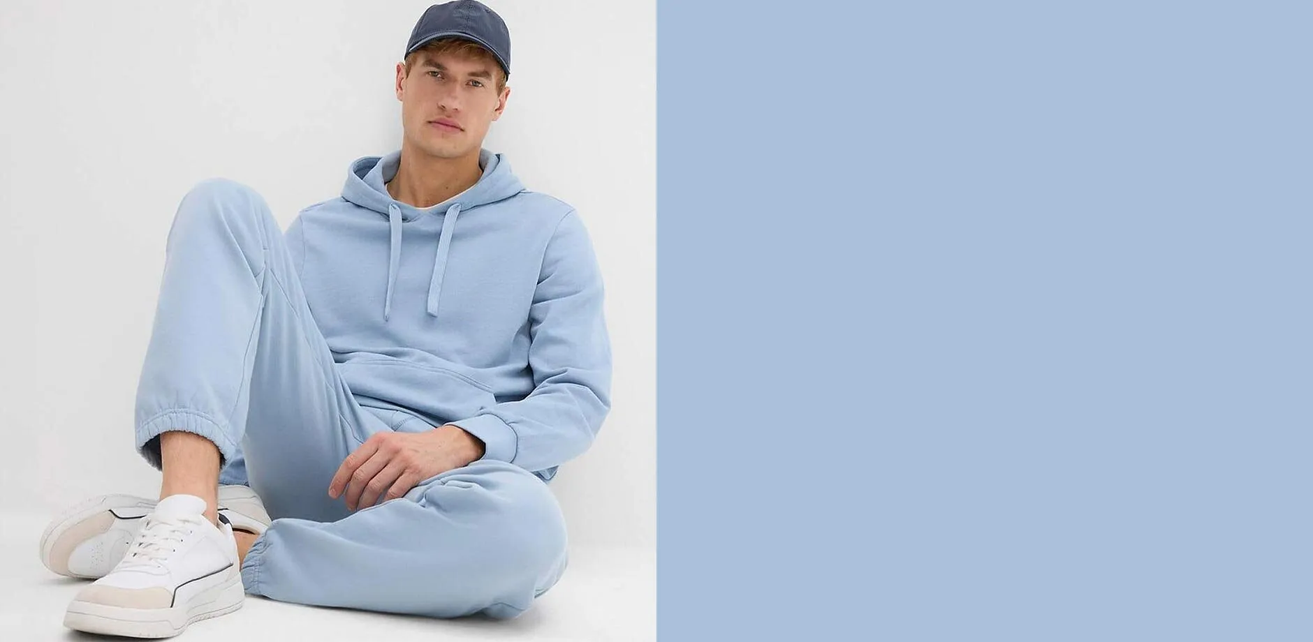 Felpa con cappuccio e pantaloni della tuta. Inoltre, scarpe da ginnastica bianche e cappellino da baseball scuro.