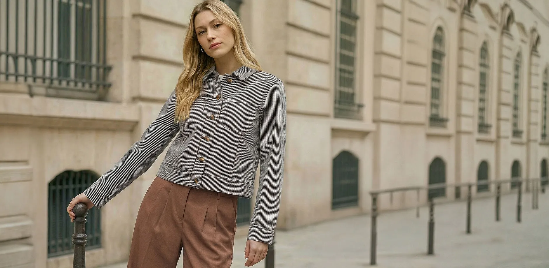 Giacca da mezza stagione a righe nere abbinata a pantaloni marroni.