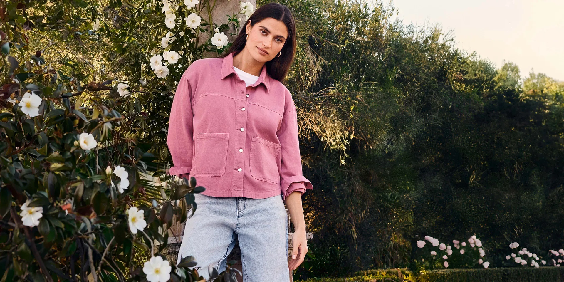 Camicia rosa con bottoni e tasche, maglietta bianca sotto, jeans chiari per un look estivo.