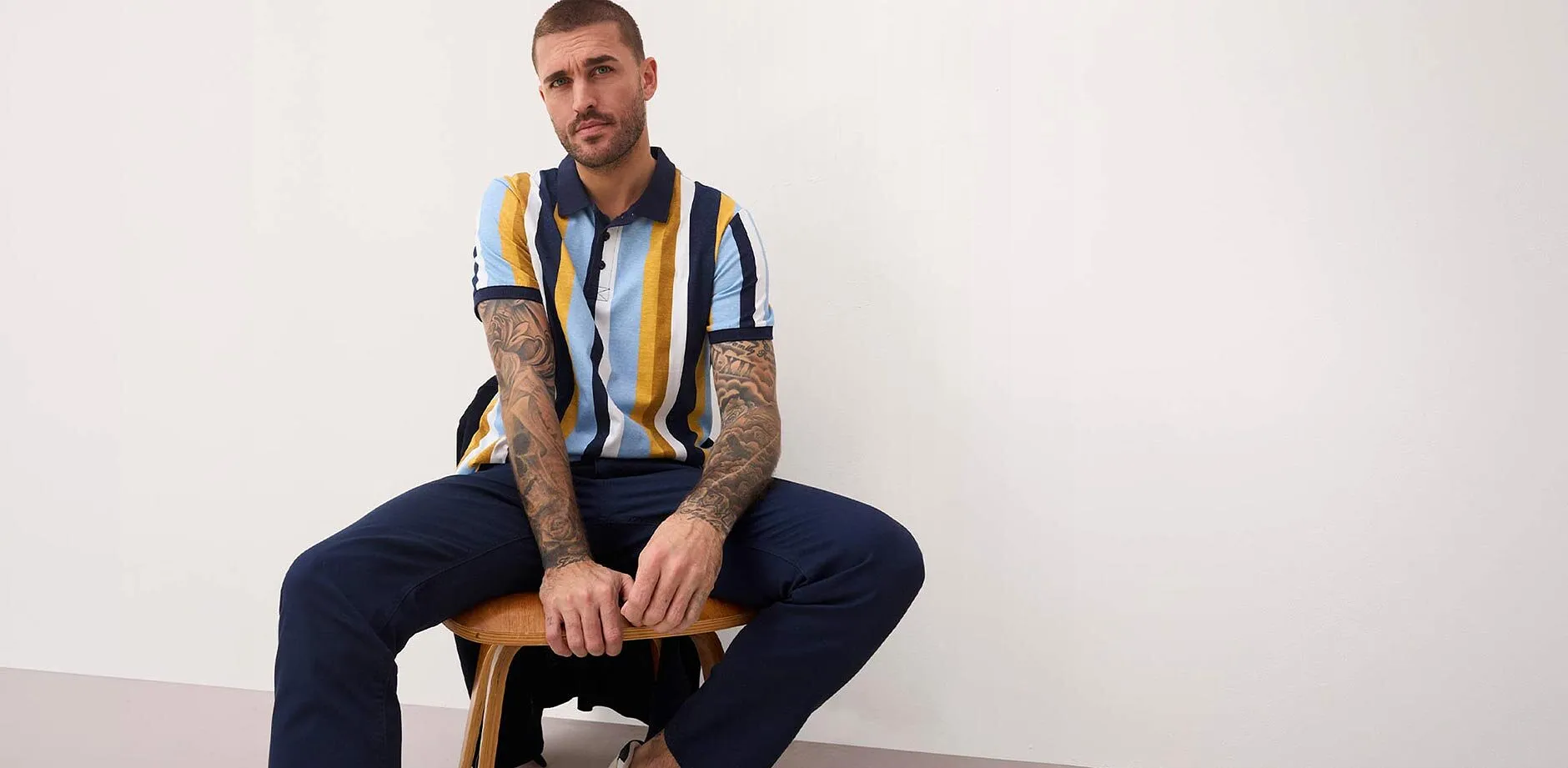 Polo a righe blu, gialle e bianche. Pantaloni blu scuro. 