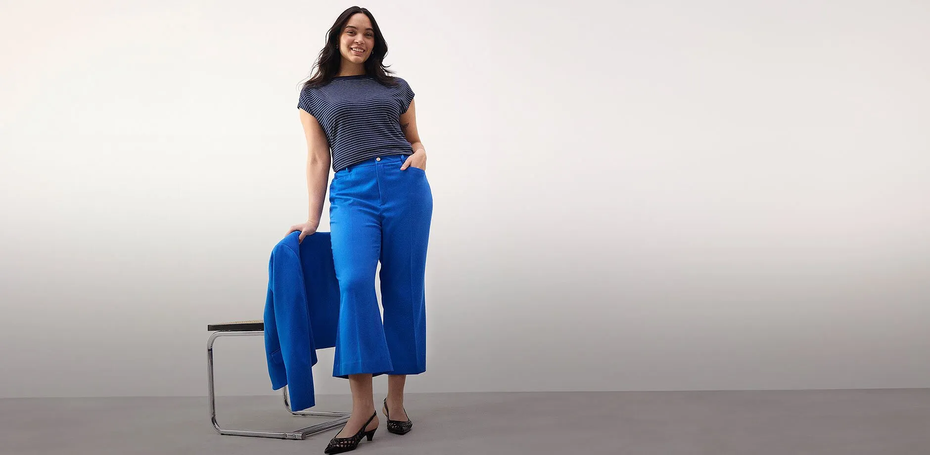 Una donna radiosa con pantaloni blu cropped e maglietta a righe.