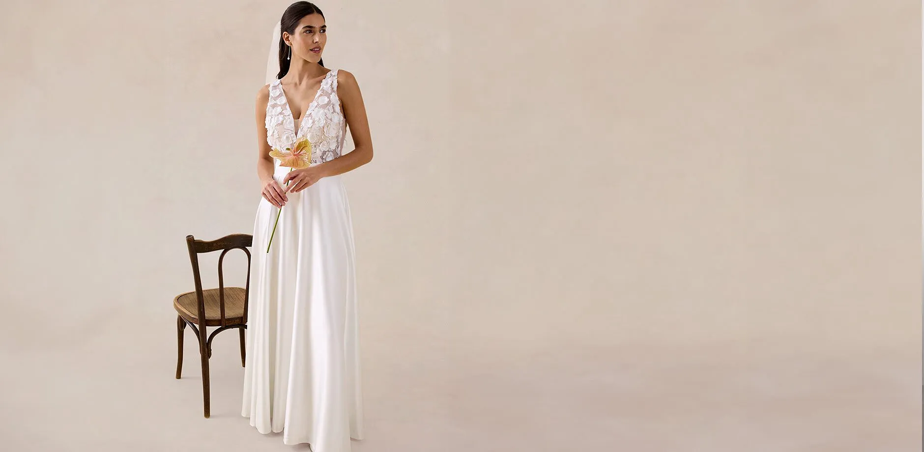 Elegante abito lungo bianco con parte superiore in pizzo, profonda scollatura a V e gonna fluida. Perfetto per i matrimoni estivi.