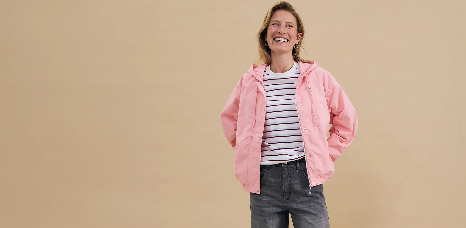 Giacca rosa sopra una maglietta a righe, abbinata a jeans grigi: un look casual per il tempo libero.