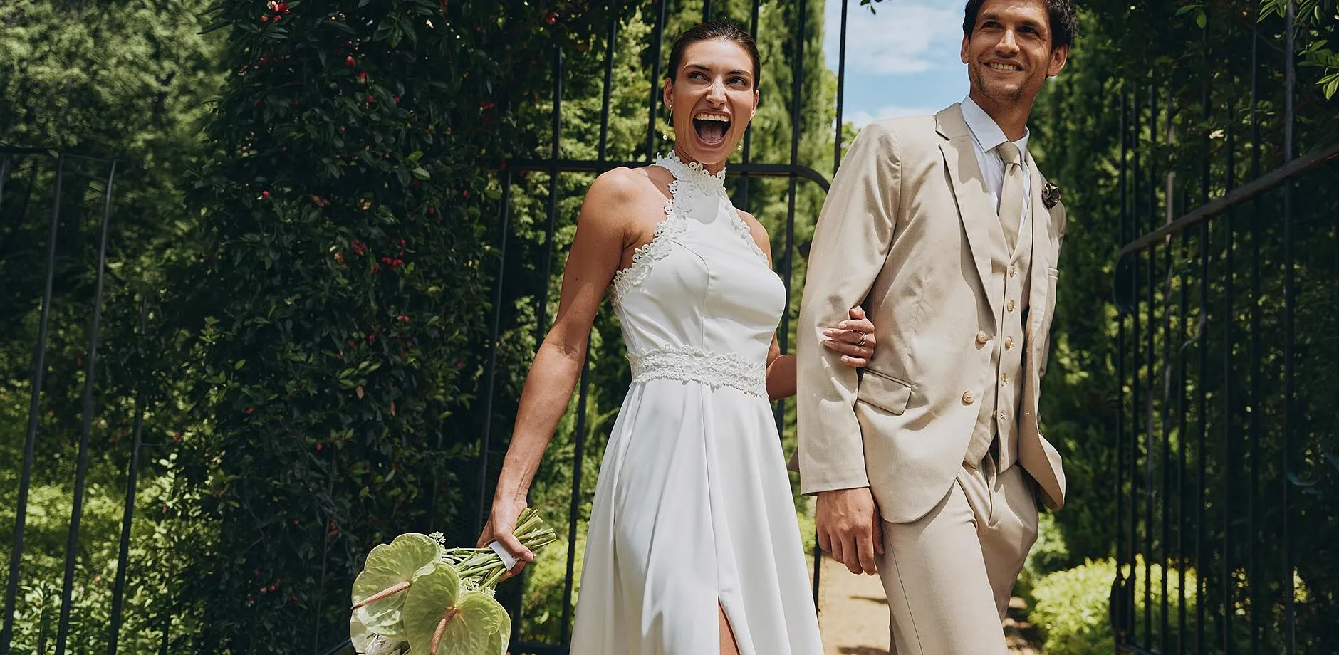 Una coppia di sposi elegante sotto il sole: lei in abito bianco, lui in abito beige