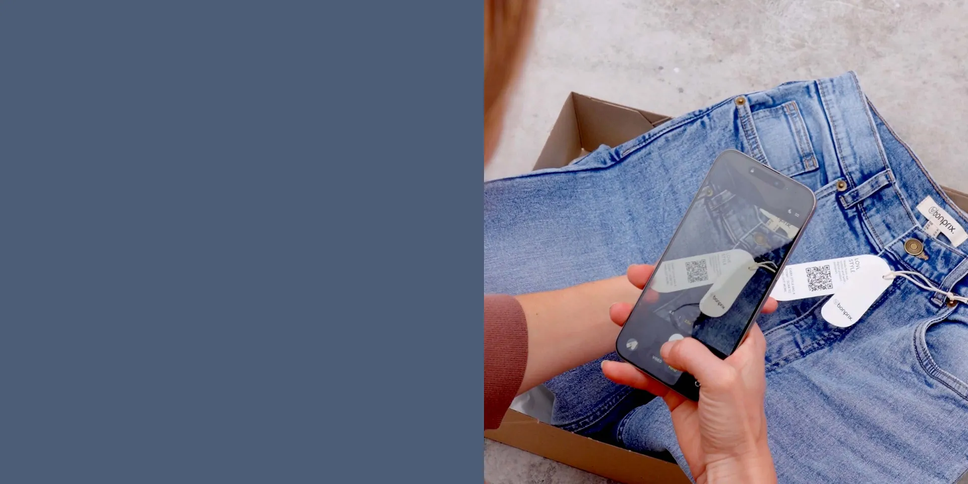 Jeans blu su uno sfondo grigio. Due mani che tengono uno smartphone sopra i vestiti.