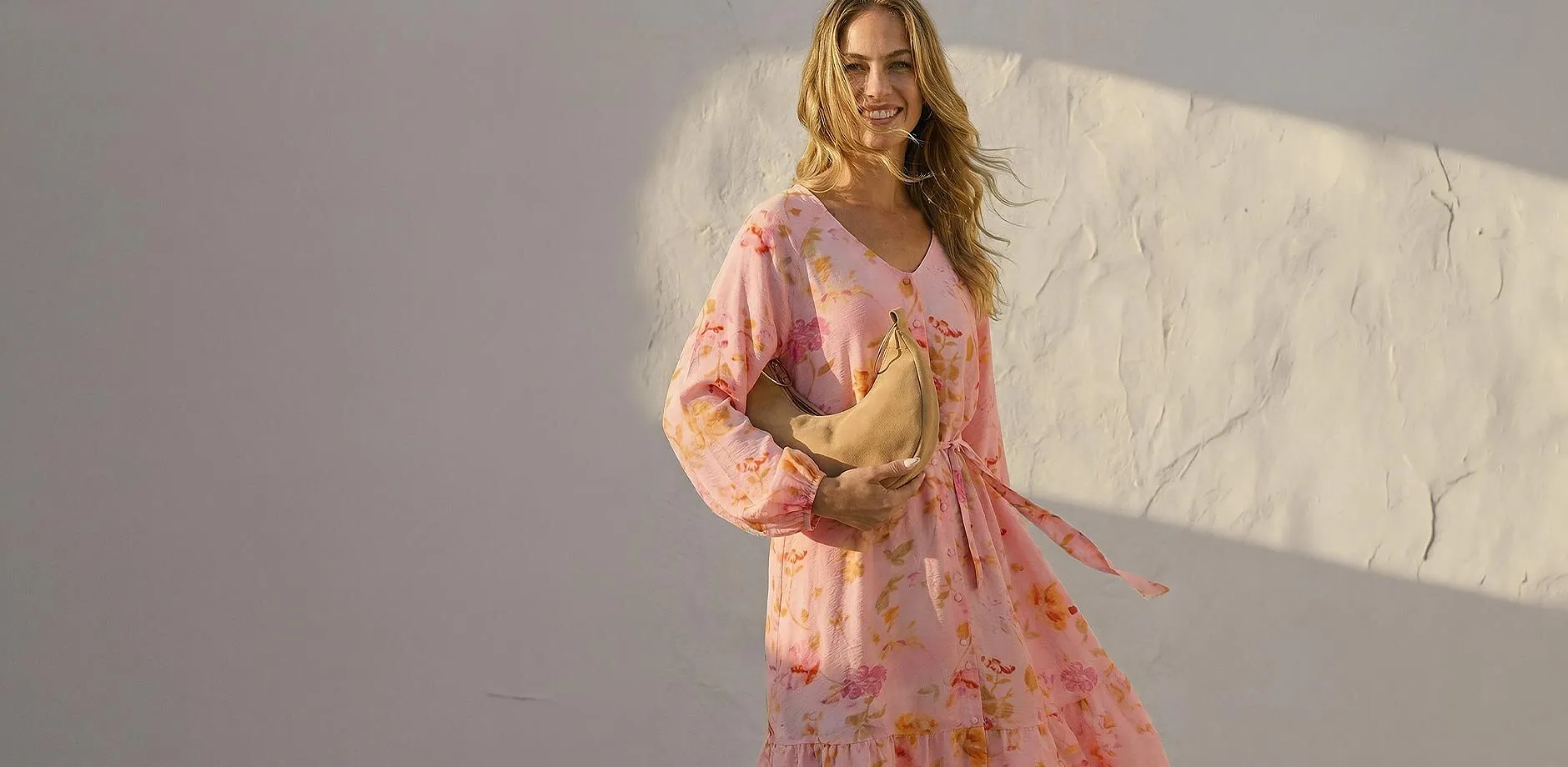 Una donna indossa un abito rosa a fiori arioso a maniche lunghe.
