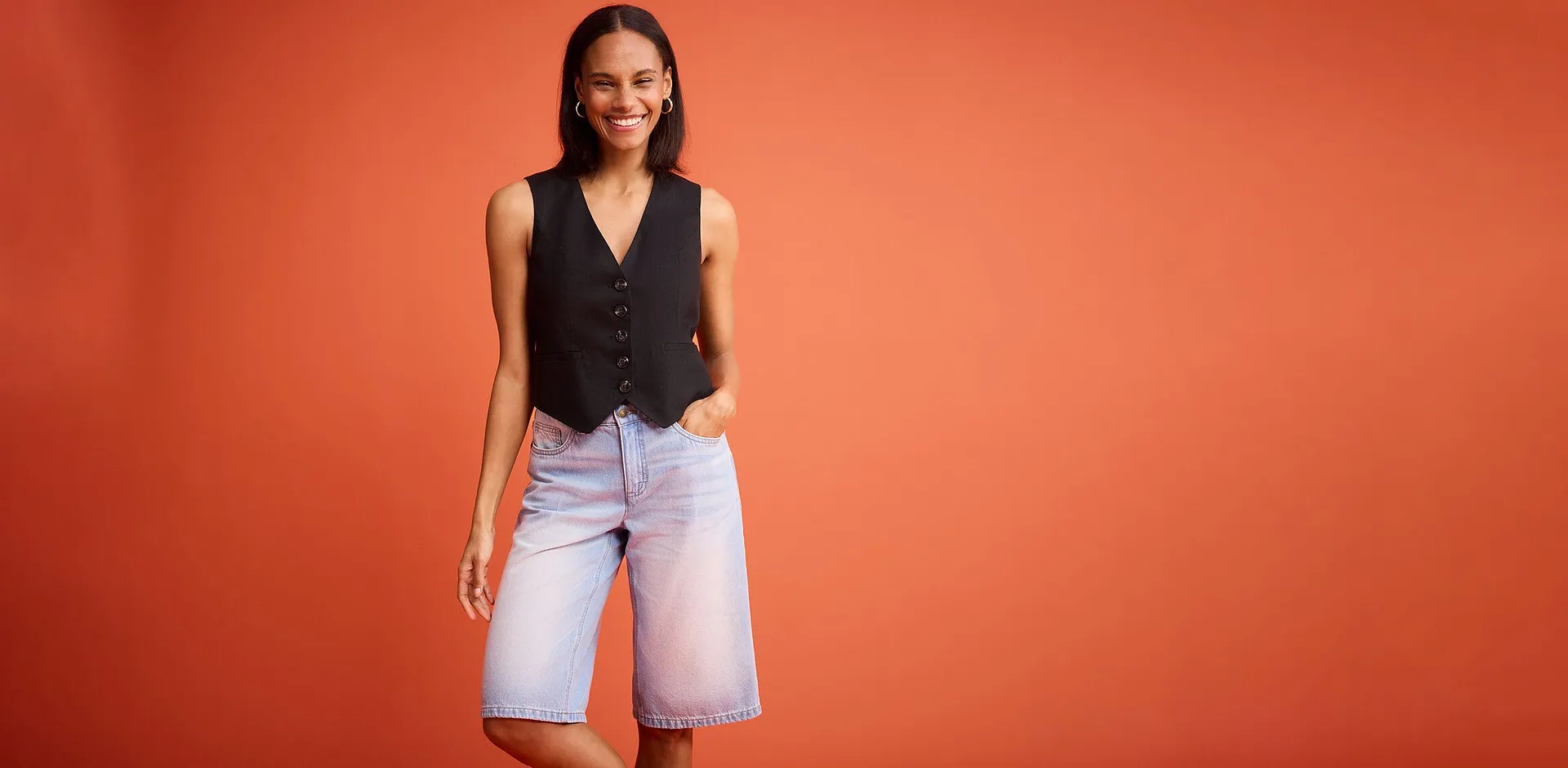 Gilet nero con bottoni abbinato a shorts di jeans azzurri.