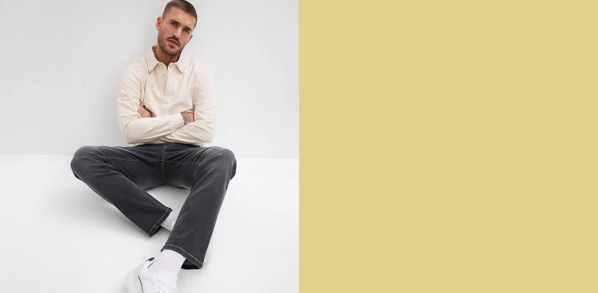 Un uomo indossa una maglietta color crema, pantaloni grigio scuro e scarpe da ginnastica bianche.