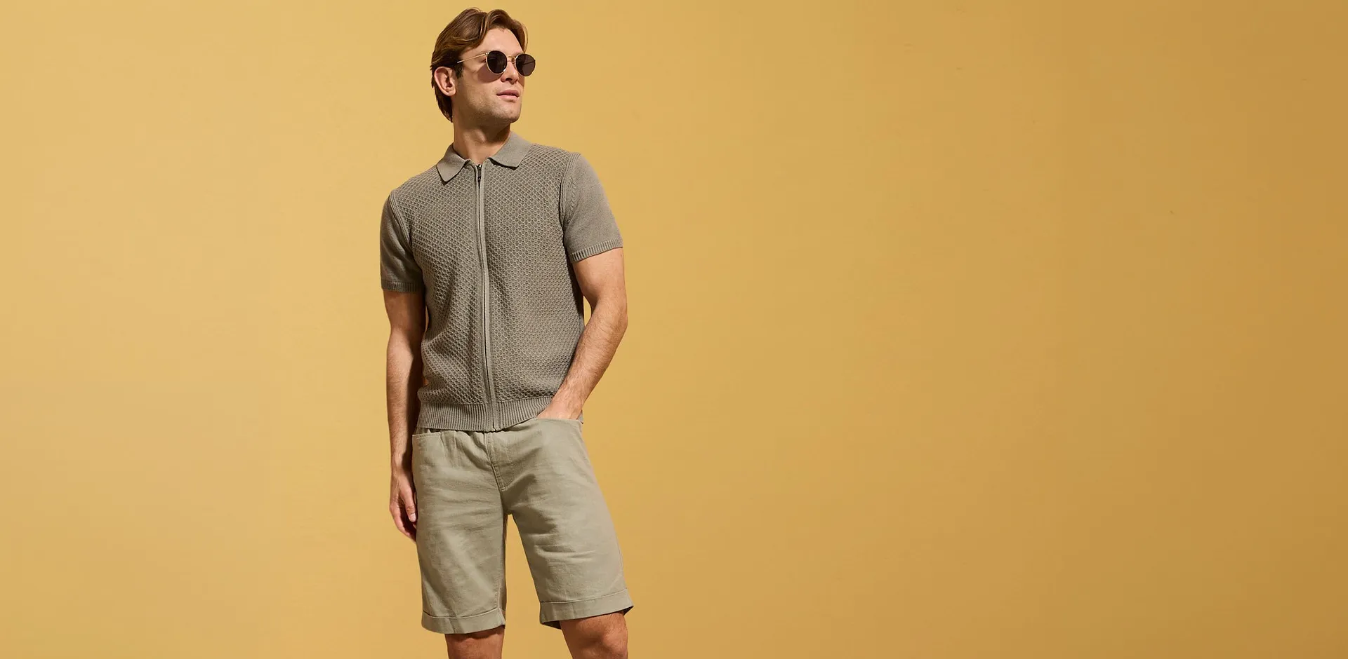 Polo grigia lavorata a maglia con cerniera e pantaloncini beige per un look estivo disinvolto.
