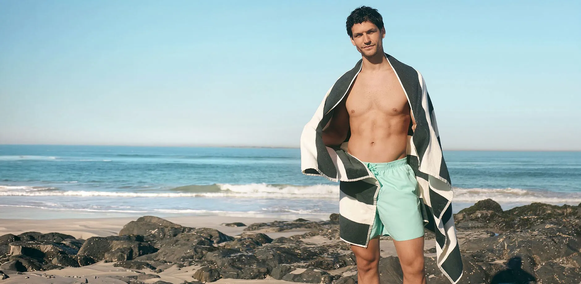 Un uomo indossa un paio di pantaloncini da bagno verde menta e ha un elegante telo da mare a righe sulle spalle.