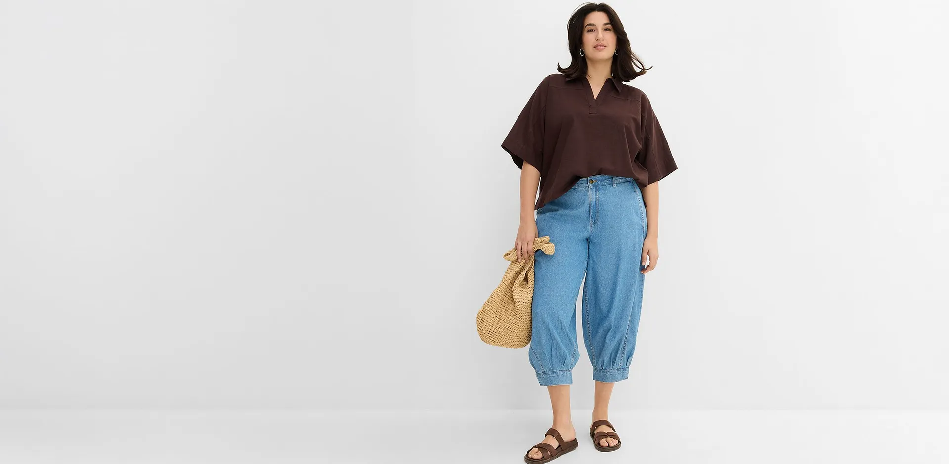Una combinazione di camicetta marrone e jeans larghi, con sandali e borsa di paglia.