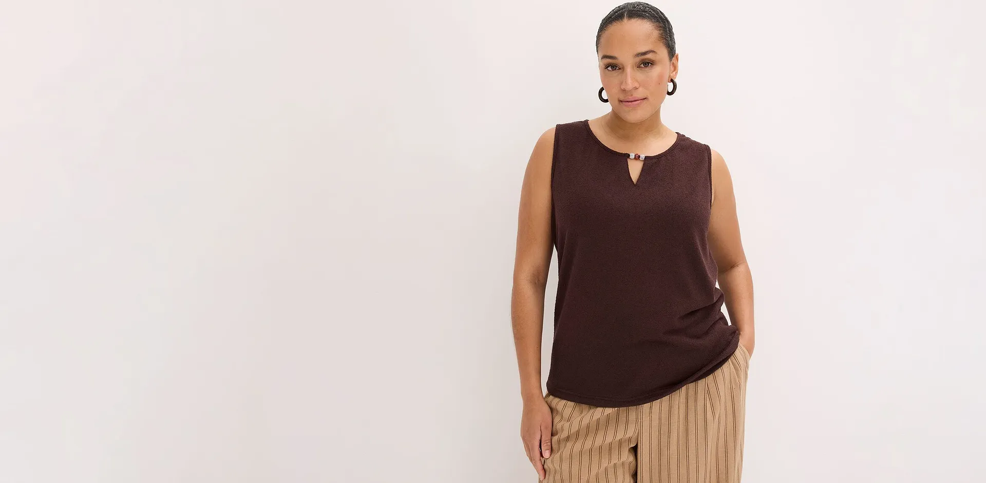 Una donna indossa un top marrone senza maniche e pantaloni a righe color beige.