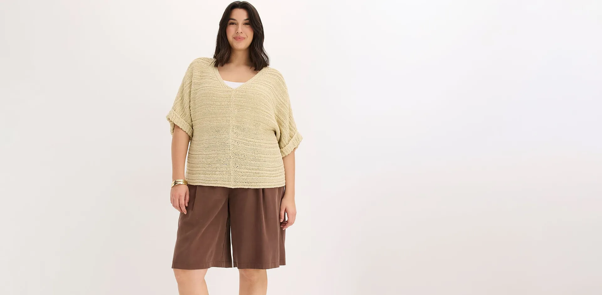 Una donna indossa un top di maglia beige e pantaloncini larghi marroni.