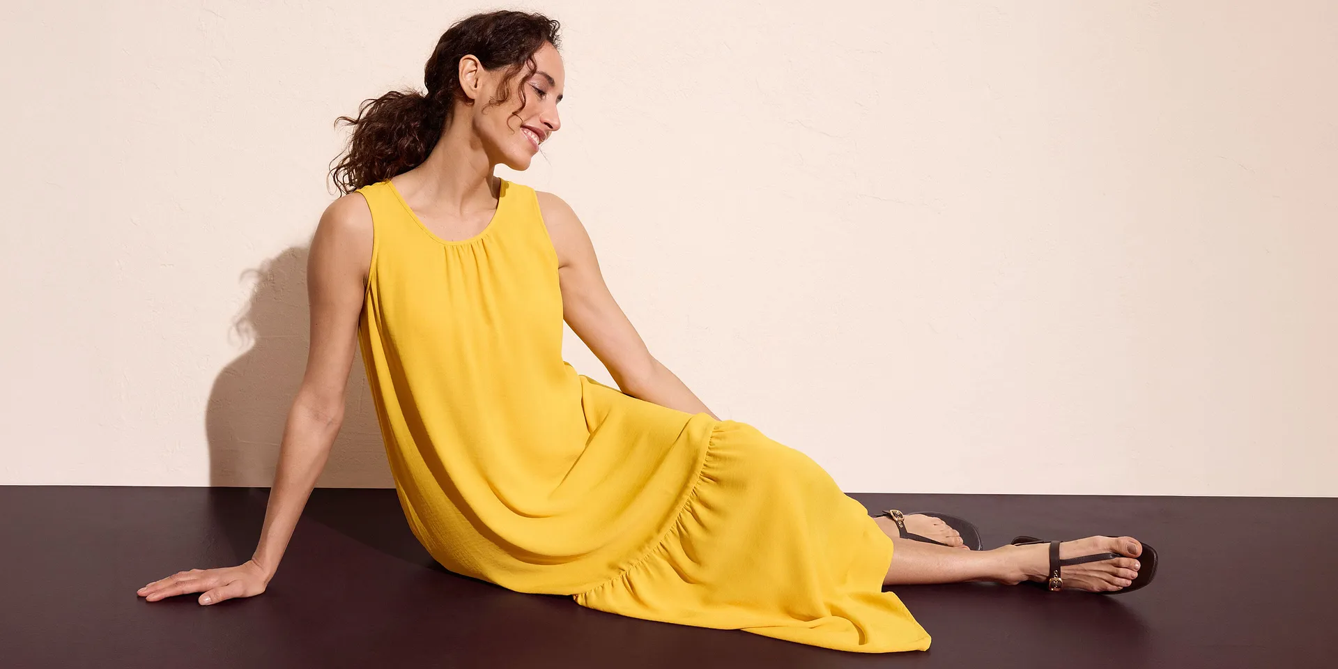 Abito lungo giallo senza maniche abbinato a sandali neri.