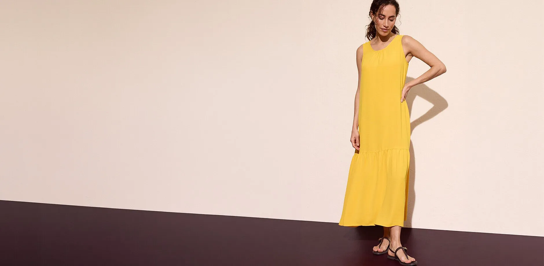 Abito lungo giallo senza maniche abbinato a sandali neri.