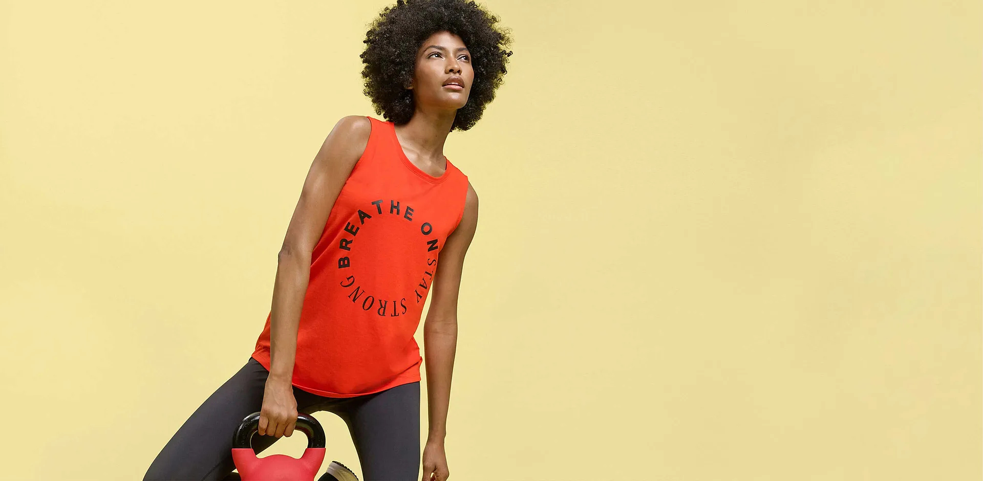 Canotta rossa con la scritta &ldquo;Breathe On Stay Strong&rdquo; e leggings scuri per l'allenamento.